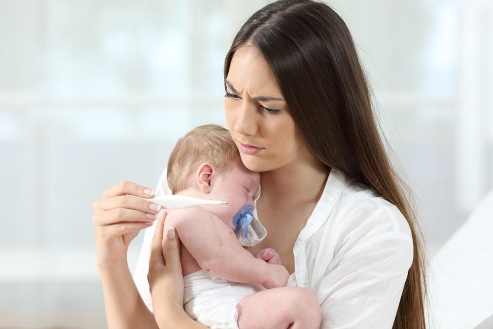 mama cu bebelus in brate citeste ingrijorata termometrul