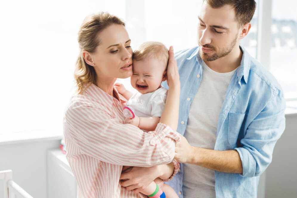 Mama si tata tin copilul in brate care a cazut din patut si plange, acestia incearca sa il linisteasca
