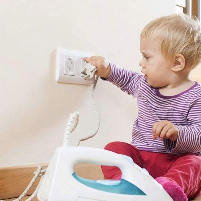 imagine cu copil mic care vrea sa bage stecherul de la fierul de calcat in priza