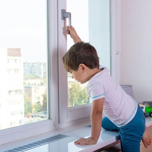 imagine cu copil care escaladeaza pervazul pentru a ajunge la geam si sta cu mana pe maner pentru a-l deschide