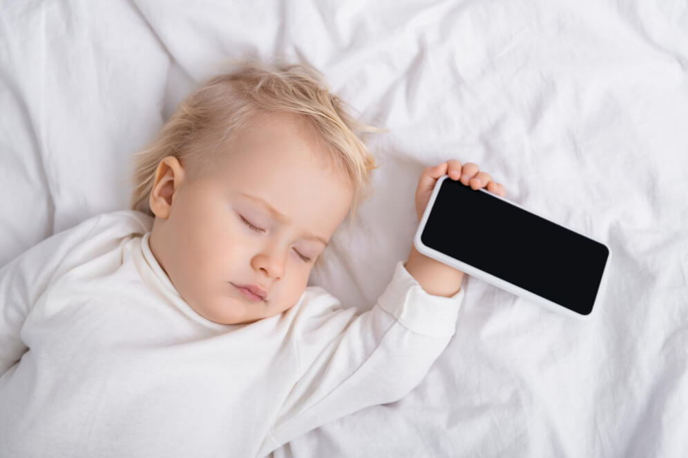 copil mic in pat cu telefonul in mana
