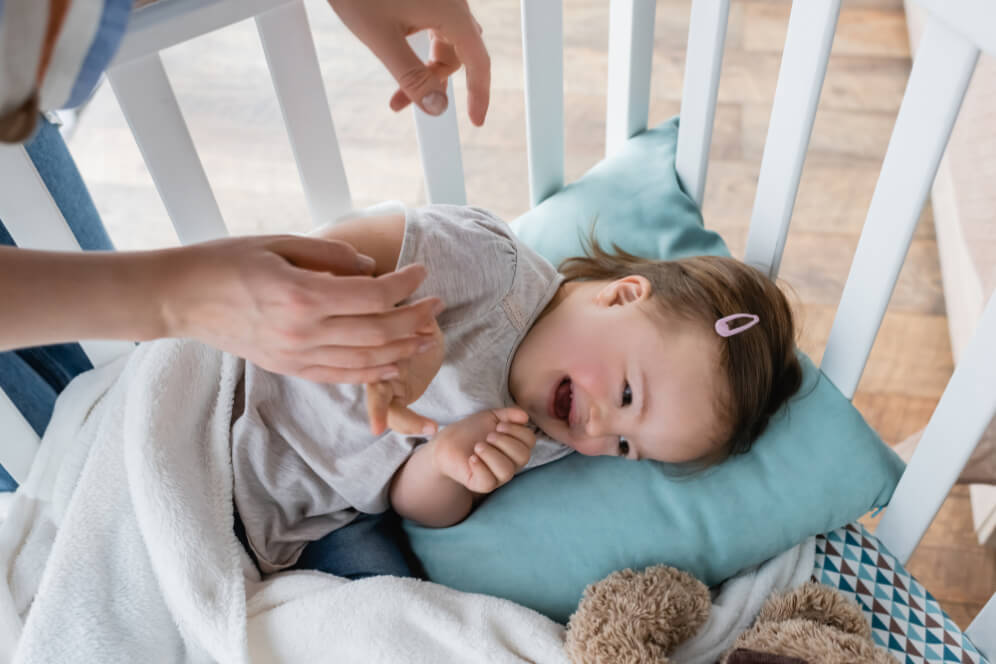 bebe fericit in patul cu gratii pentru copii