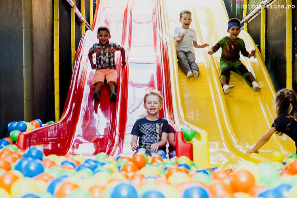 imagine colorata cu mai multi copii care coboara pe tobogan intr-o piscina cu bile