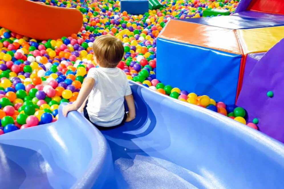 imagine colorata cu mai multi copii care coboara pe tobogan intr-o piscina cu bile