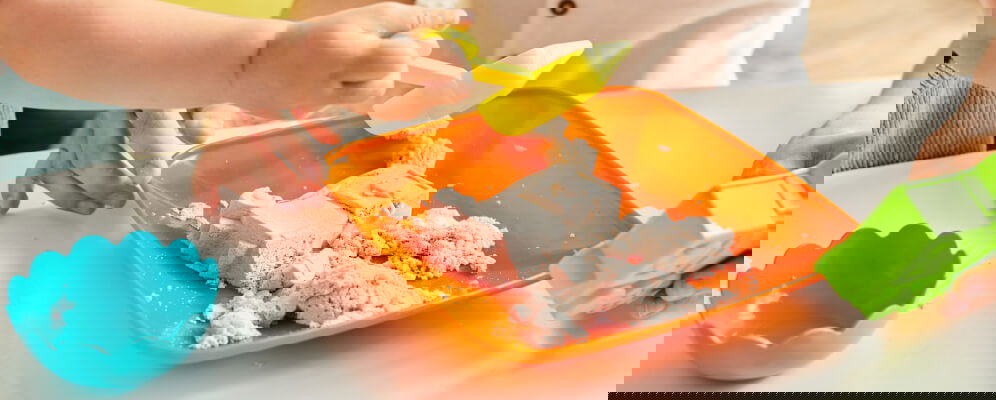 maini de copil care se joaca cu plastilina coloarata pe masa