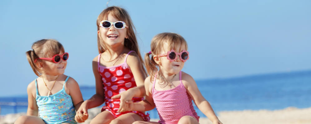 trei fetite la plaja se tin de maini si au ochelari de soare