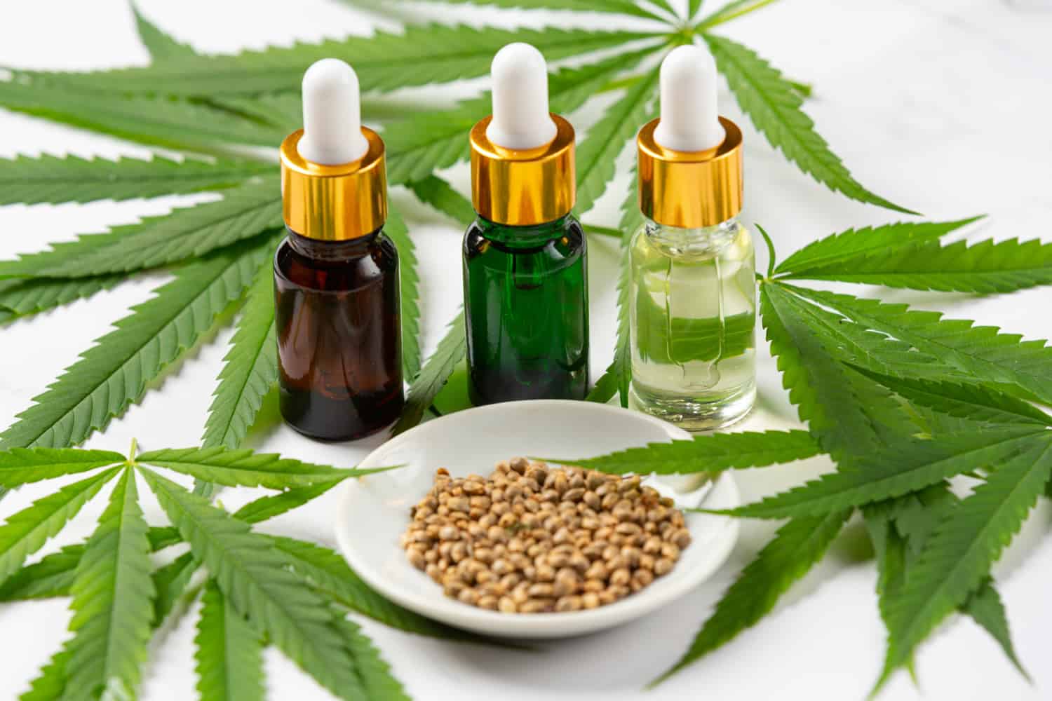 2. ulei cbd oboseala. sticlute de ulei bruna, verde si transparenta, frunze de canepa, farfurie cu seminte