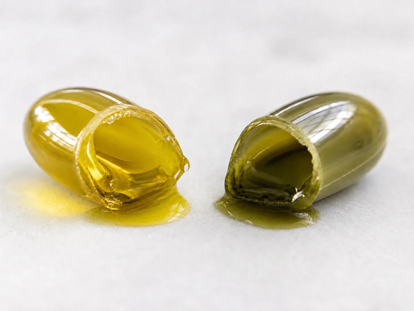 Două capsule softgel deschise care arată diferența de culoare între uleiul de cânepă alimentar și extractul de canabis full spectrum