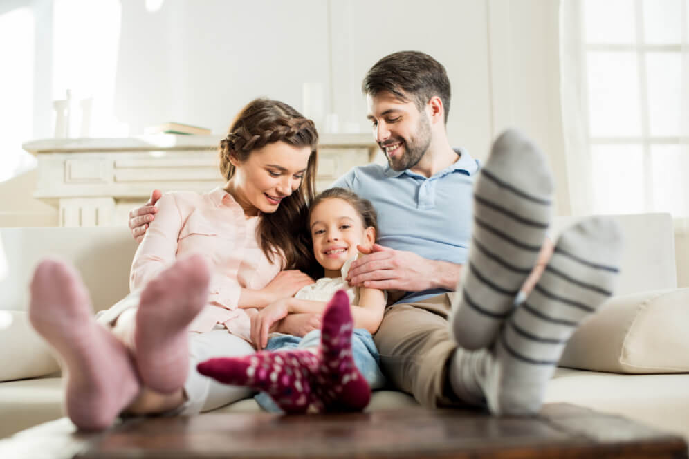 mama fetita si tata stau cu picioarele pe masa in sufragerie relaxati si zambesc